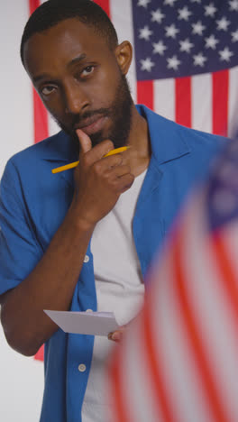 Vertical-Video-Shot-Of-Man-Stands-At-Ballot-Box-In-American-Election-Deciding-How-To-Cast-His-Vote